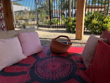 Outdoor cubby looking towards the neighbouring community garden. This space includes cushions, mat and basket of books.